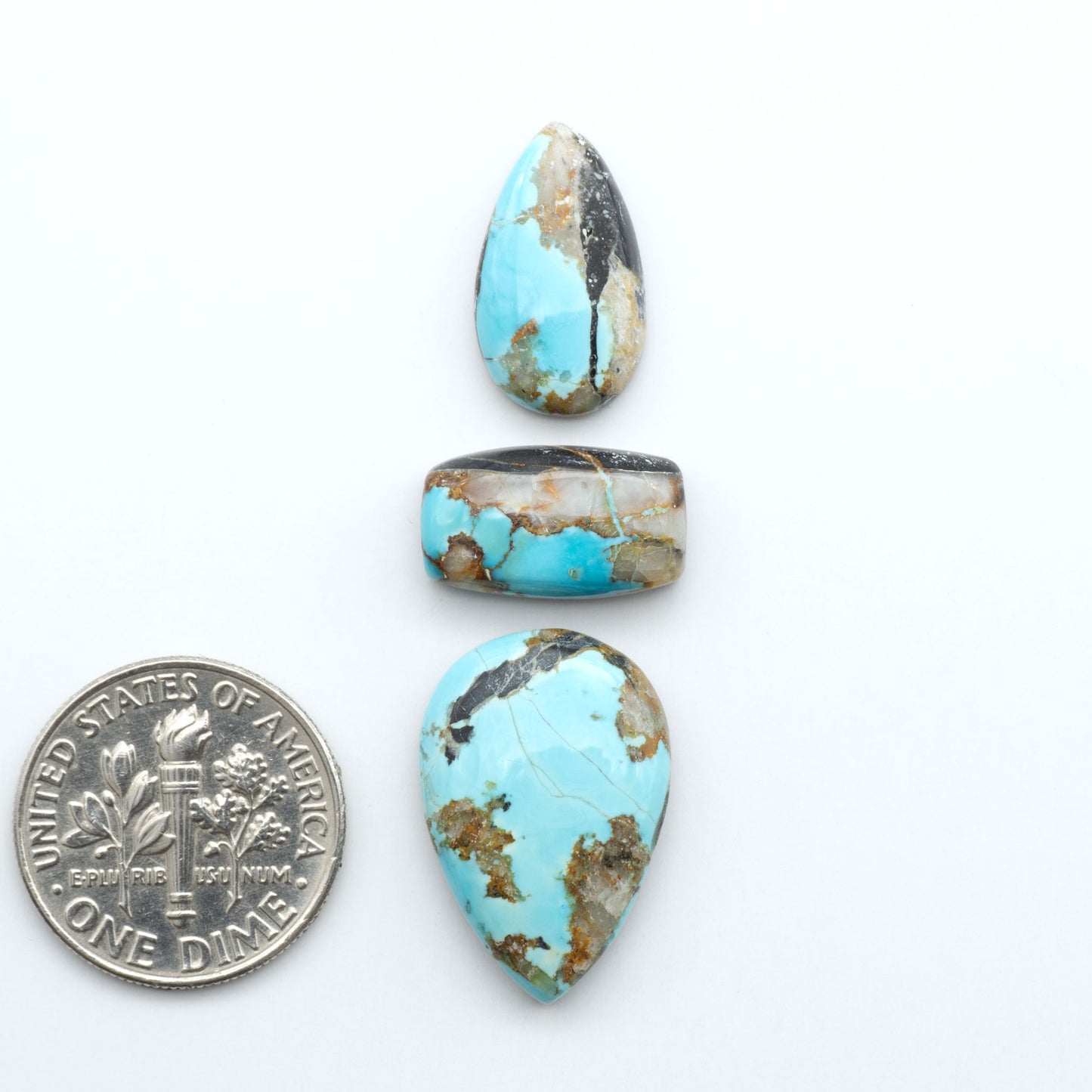 Black Jack turquoise cabochons, blue-green color with black matrix, polished stones on a white background with a US dime for scale