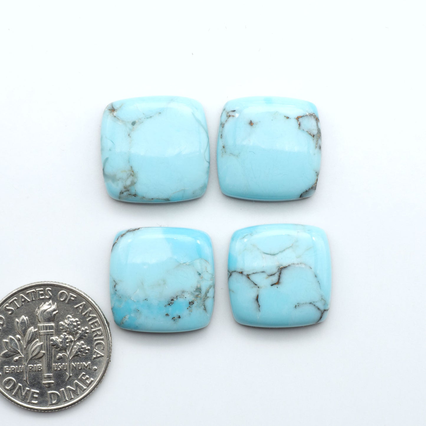 Pressed Turquoise nugget cabochons, composite material with a blue color and dark matrix on a white background, with a US dime for scale.