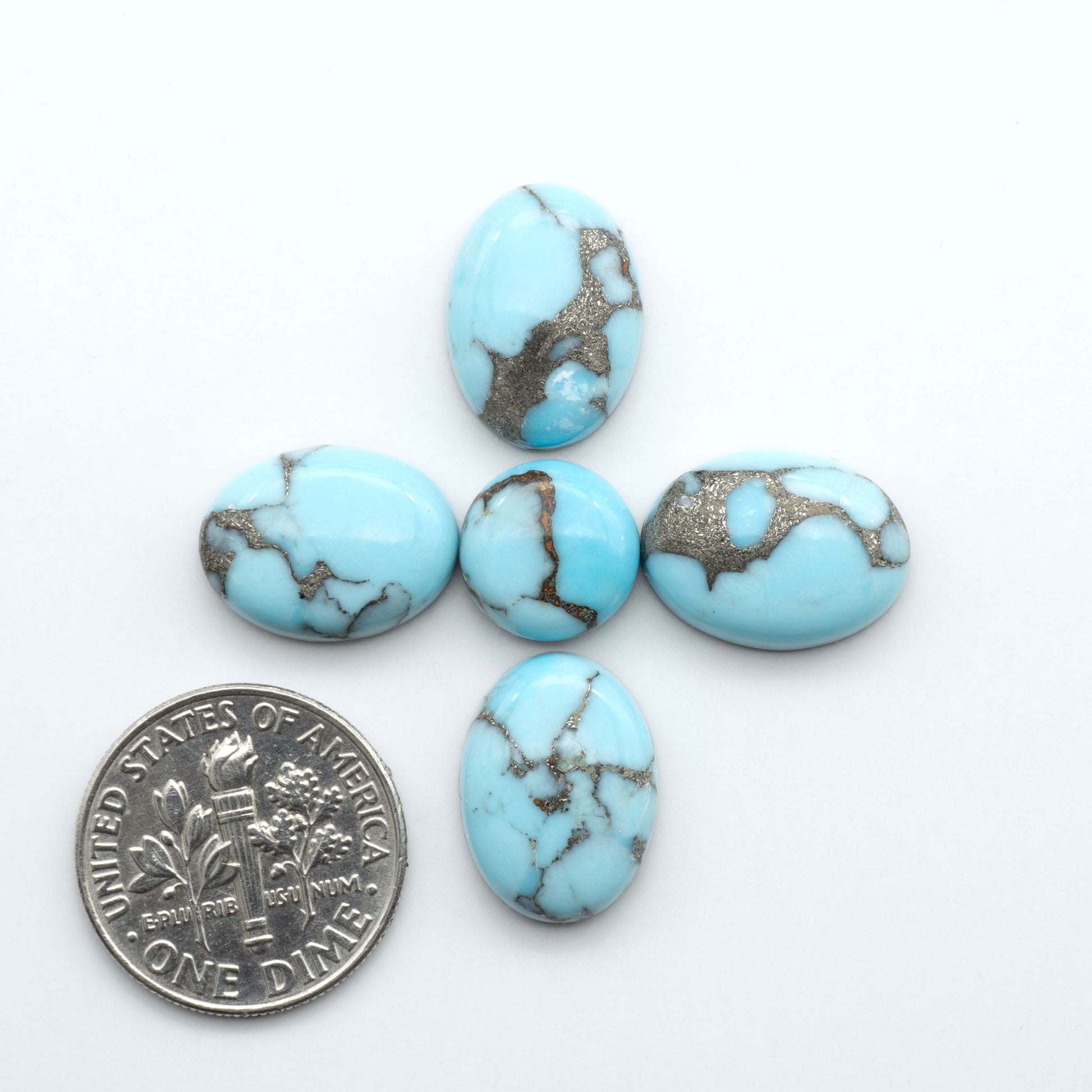 Pressed Turquoise nugget cabochons, composite material with a blue color and dark matrix on a white background, with a US dime for scale.
