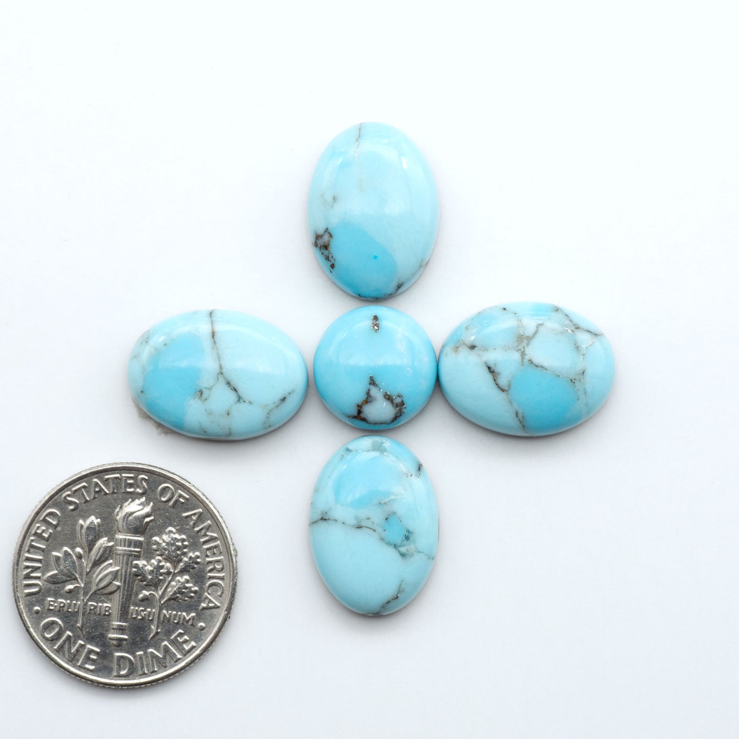 Pressed Turquoise nugget cabochons, composite material with a blue color and dark matrix on a white background, with a US dime for scale.