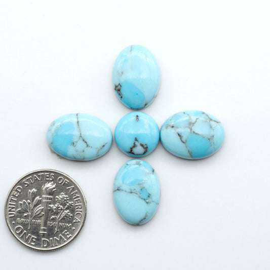 Pressed Turquoise nugget cabochons, composite material with a blue color and dark matrix on a white background, with a US dime for scale.