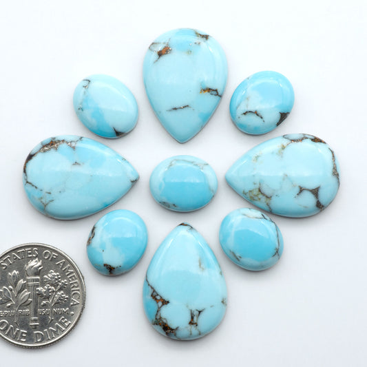 Pressed Turquoise nugget cabochons, composite material with a blue color and dark matrix on a white background, with a US dime for scale.