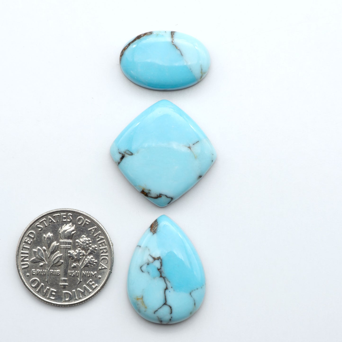 Pressed Turquoise nugget cabochons, composite material with a blue color and dark matrix on a white background, with a US dime for scale.