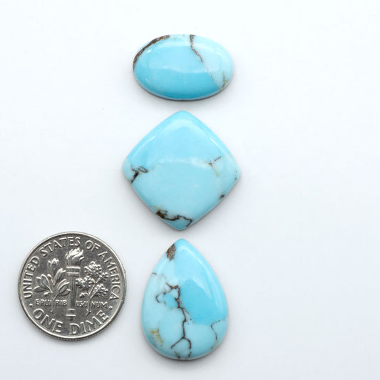 Pressed Turquoise nugget cabochons, composite material with a blue color and dark matrix on a white background, with a US dime for scale.