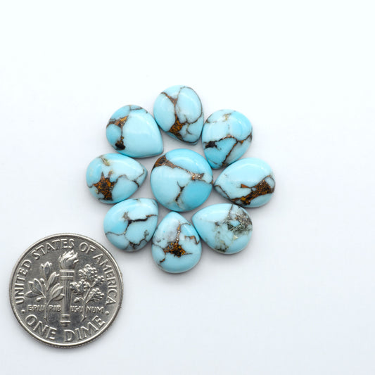 Pressed Turquoise nugget cabochons, composite material with a blue color and dark matrix on a white background, with a US dime for scale.