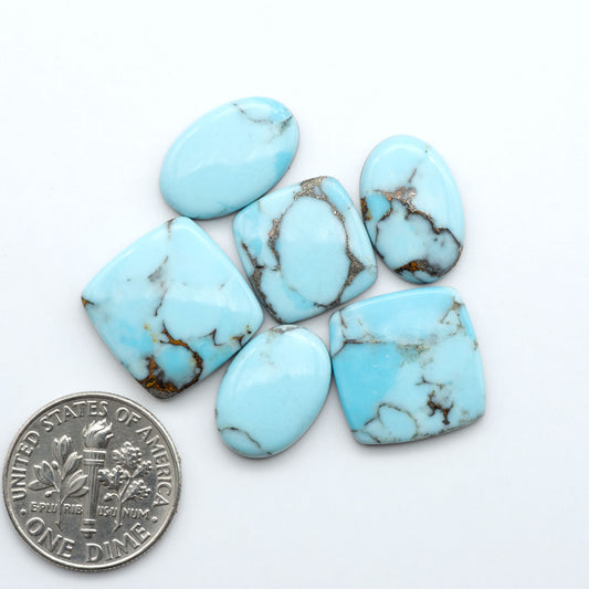 Pressed Turquoise nugget cabochons, composite material with a blue color and dark matrix on a white background, with a US dime for scale.