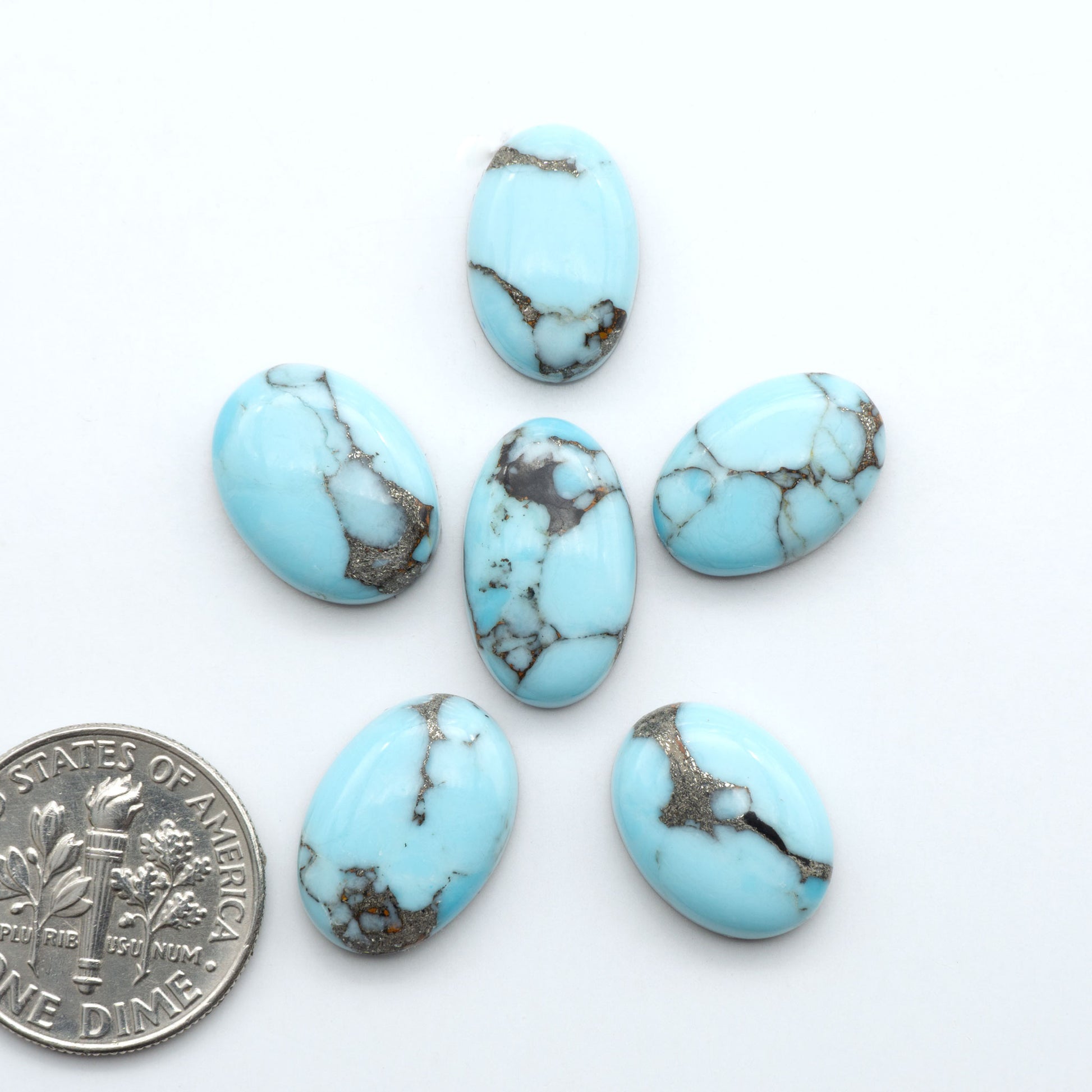 Pressed Turquoise nugget cabochons, composite material with a blue color and dark matrix on a white background, with a US dime for scale.