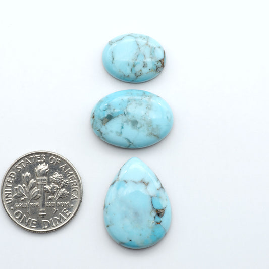 Pressed Turquoise nugget cabochons, composite material with a blue color and dark matrix on a white background, with a US dime for scale.
