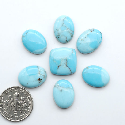 Pressed Turquoise nugget cabochons, composite material with a blue color and dark matrix on a white background, with a US dime for scale.