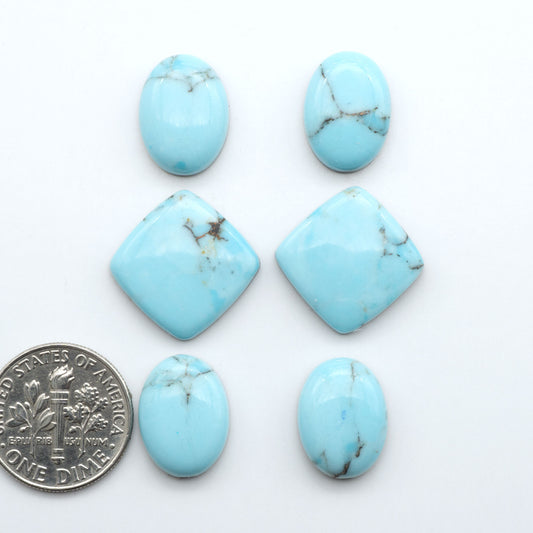 Pressed Turquoise nugget cabochons, composite material with a blue color and dark matrix on a white background, with a US dime for scale.