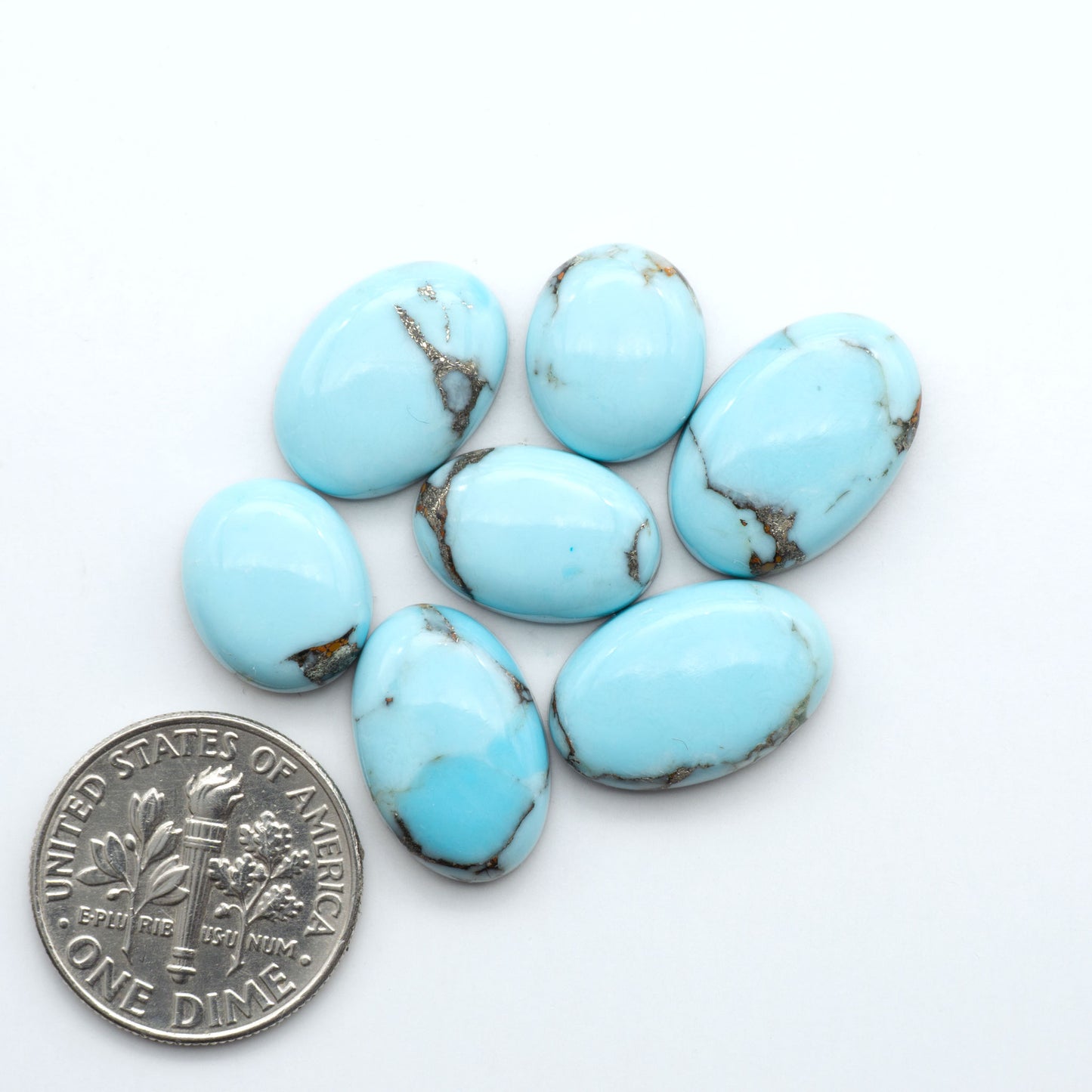Pressed Turquoise nugget cabochons, composite material with a blue color and dark matrix on a white background, with a US dime for scale.