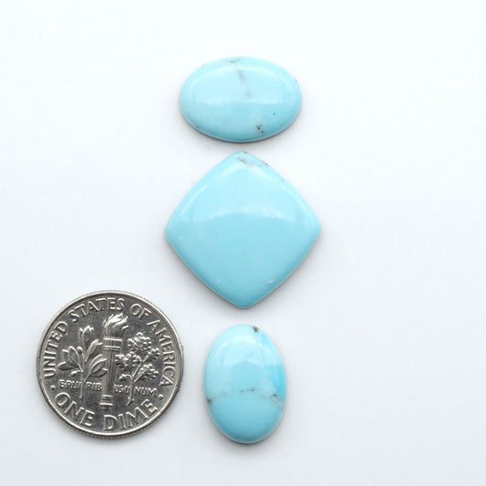 Pressed Turquoise nugget cabochons, composite material with a blue color and dark matrix on a white background, with a US dime for scale.