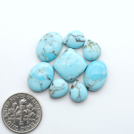 Pressed Turquoise nugget cabochons, composite material with a blue color and dark matrix on a white background, with a US dime for scale.