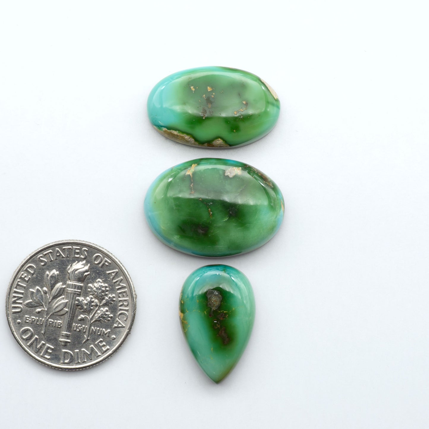 Sonoran Mountain Turquoise cabochons, blue-green color with natural matrix, polished stones on a white background, with a US dime for scale