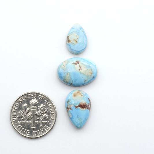 Golden Hills Turquoise cabochons, icy blue to lavender tones with chocolate matrix, polished stones on a white background with a US dime for scale