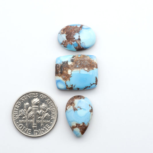 Golden Hills Turquoise cabochons, icy blue to lavender tones with chocolate matrix, polished stones on a white background with a US dime for scale