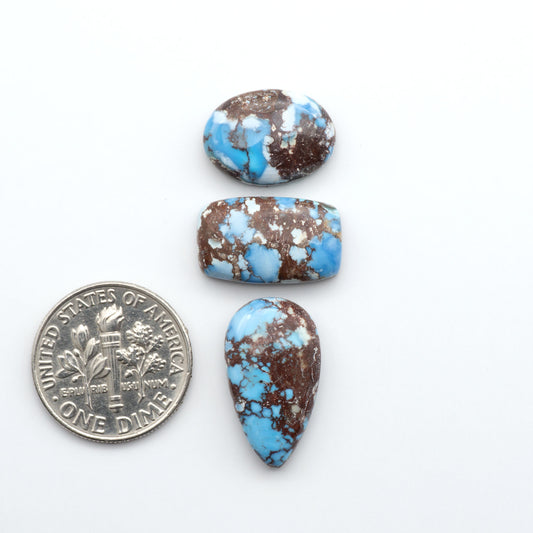 Golden Hills Turquoise cabochons, icy blue to lavender tones with chocolate matrix, polished stones on a white background with a US dime for scale