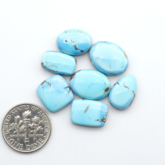 Golden Hills Turquoise cabochons, icy blue to lavender tones with chocolate matrix, polished stones on a white background with a US dime for scale