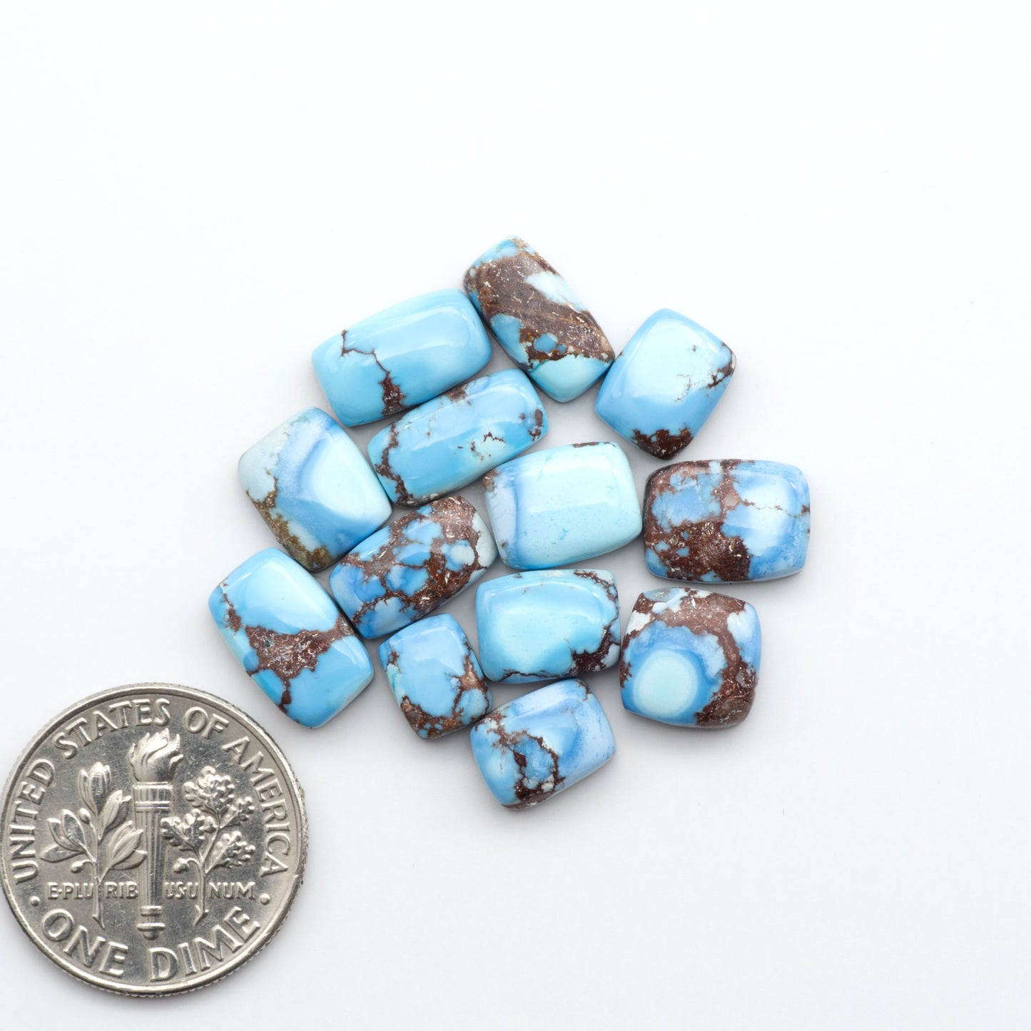 Golden Hills Turquoise cabochons, icy blue to lavender tones with chocolate matrix, polished stones on a white background with a US dime for scale