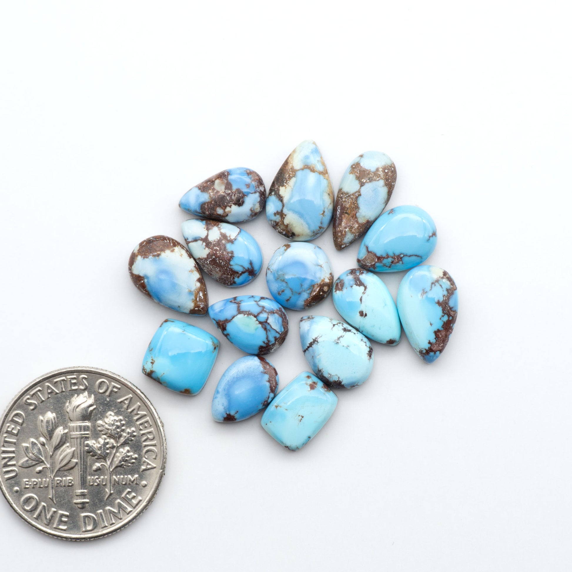 Golden Hills Turquoise cabochons, icy blue to lavender tones with chocolate matrix, polished stones on a white background with a US dime for scale