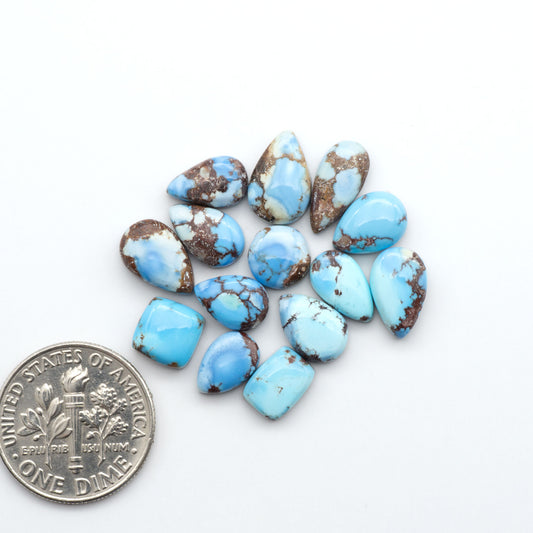 Golden Hills Turquoise cabochons, icy blue to lavender tones with chocolate matrix, polished stones on a white background with a US dime for scale