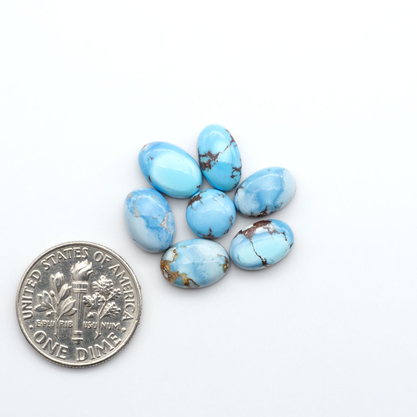 Golden Hills Turquoise cabochons, icy blue to lavender tones with chocolate matrix, polished stones on a white background with a US dime for scale