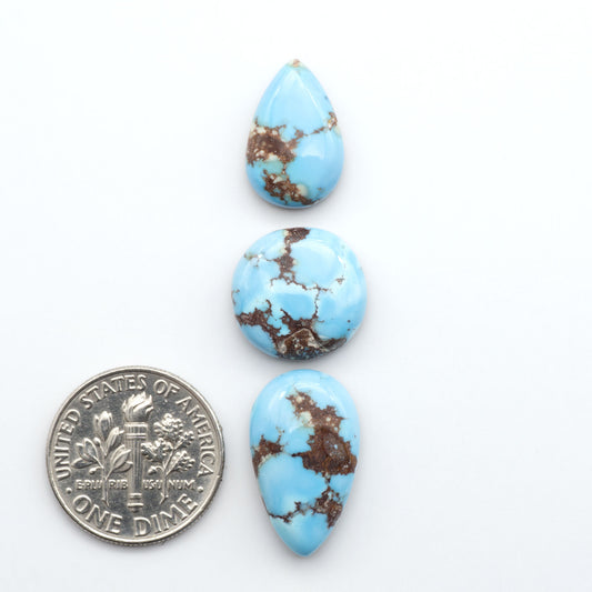 Golden Hills Turquoise cabochons, icy blue to lavender tones with chocolate matrix, polished stones on a white background with a US dime for scale