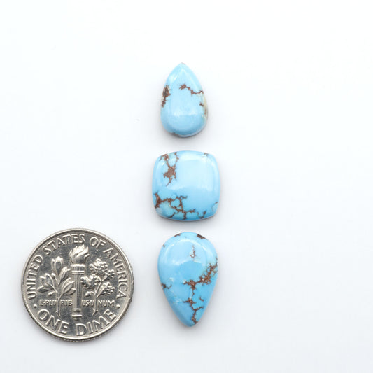 Golden Hills Turquoise cabochons, icy blue to lavender tones with chocolate matrix, polished stones on a white background with a US dime for scale