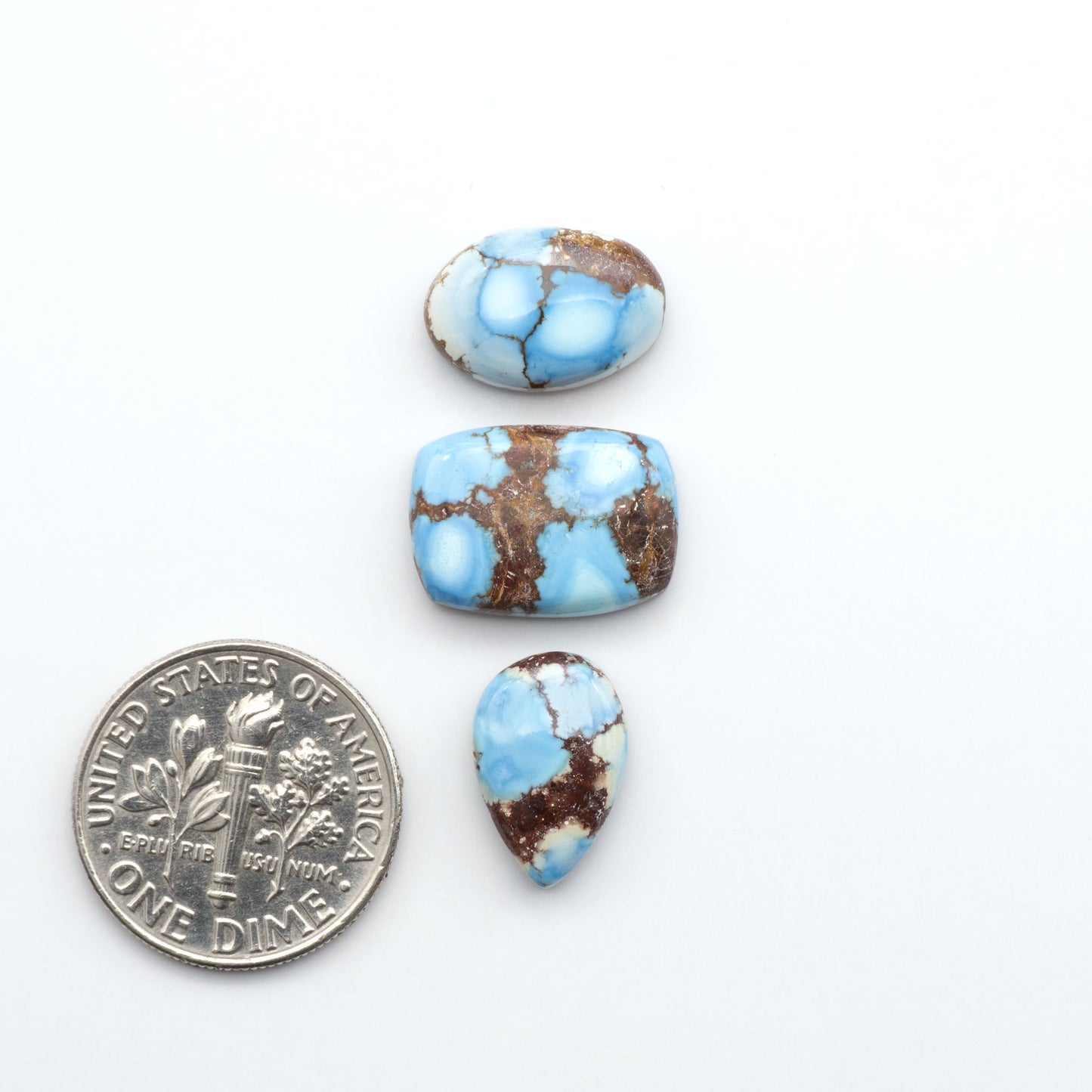 Golden Hills Turquoise cabochons, icy blue to lavender tones with chocolate matrix, polished stones on a white background with a US dime for scale