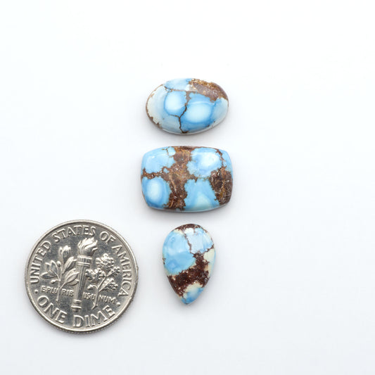 Golden Hills Turquoise cabochons, icy blue to lavender tones with chocolate matrix, polished stones on a white background with a US dime for scale