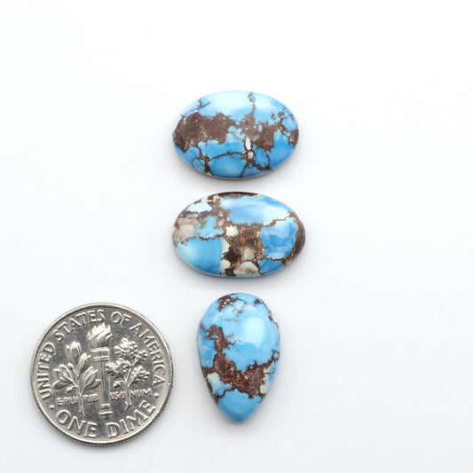 Golden Hills Turquoise cabochons, icy blue to lavender tones with chocolate matrix, polished stones on a white background with a US dime for scale