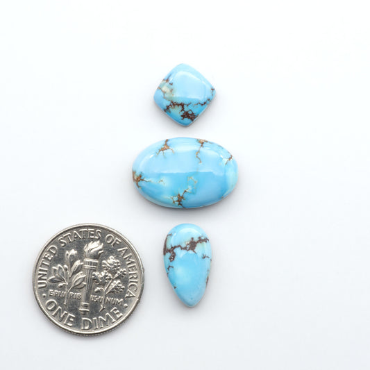 Golden Hills Turquoise cabochons, icy blue to lavender tones with chocolate matrix, polished stones on a white background with a US dime for scale