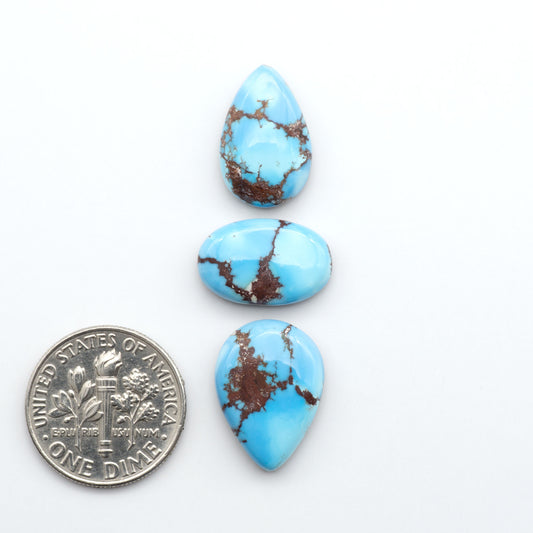 Golden Hills Turquoise cabochons, icy blue to lavender tones with chocolate matrix, polished stones on a white background with a US dime for scale