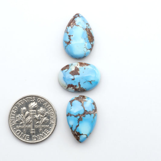 Golden Hills Turquoise cabochons, icy blue to lavender tones with chocolate matrix, polished stones on a white background with a US dime for scale