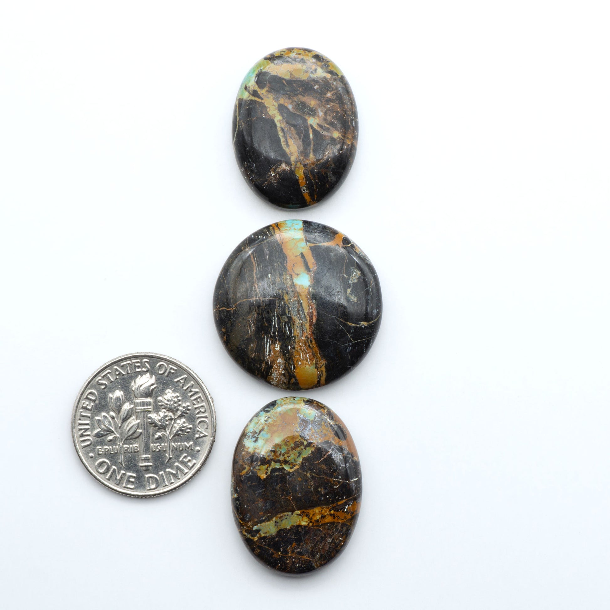 Black Jack turquoise cabochons, blue-green color with black matrix, polished stones on a white background with a US dime for scale