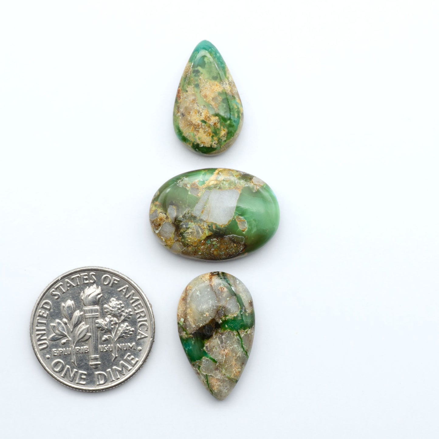 Sonoran Mountain Turquoise cabochons, blue-green color with natural matrix, polished stones on a white background, with a US dime for scale