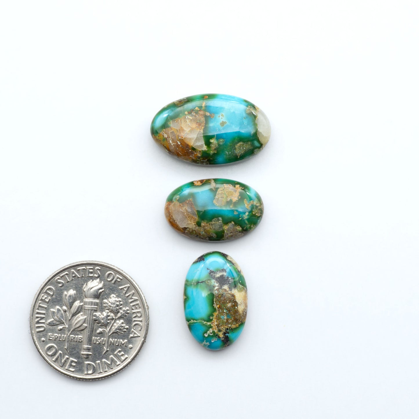 Sonoran Mountain Turquoise cabochons, blue-green color with natural matrix, polished stones on a white background, with a US dime for scale