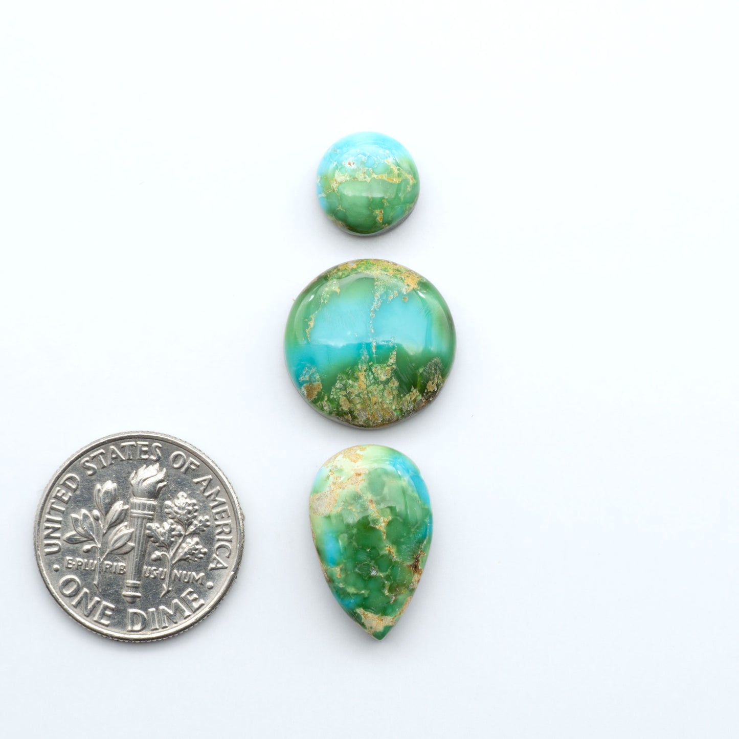 Sonoran Mountain Turquoise cabochons, blue-green color with natural matrix, polished stones on a white background, with a US dime for scale