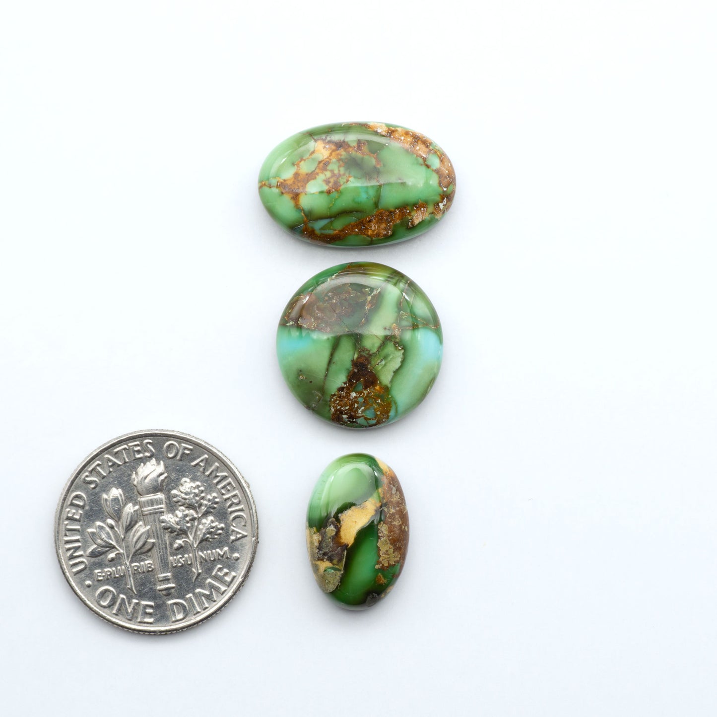 Sonoran Mountain Turquoise cabochons, blue-green color with natural matrix, polished stones on a white background, with a US dime for scale