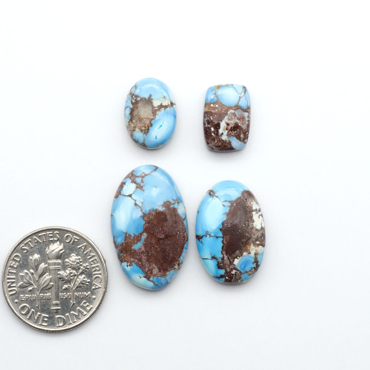 Golden Hills Turquoise cabochons, icy blue to lavender tones with chocolate matrix, polished stones on a white background with a US dime for scale