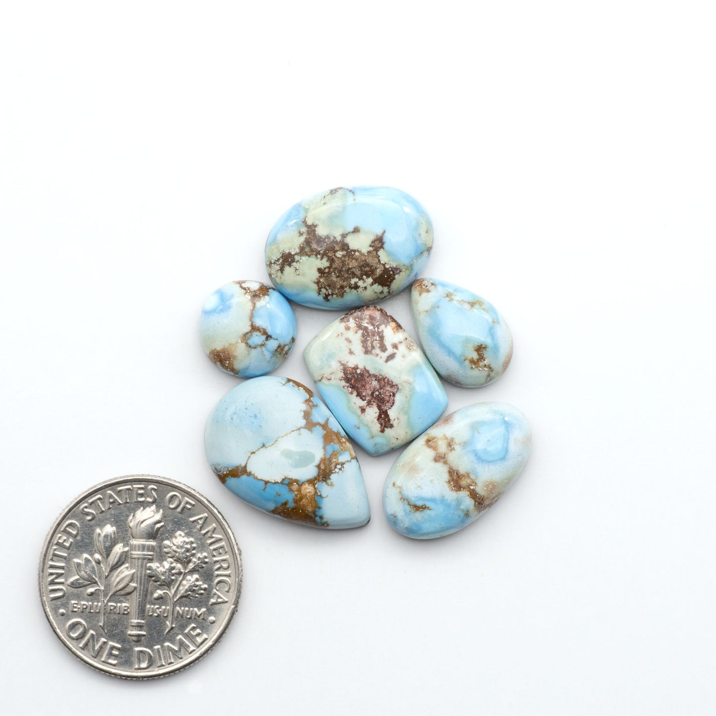 Golden Hills Turquoise cabochons, icy blue to lavender tones with chocolate matrix, polished stones on a white background with a US dime for scale