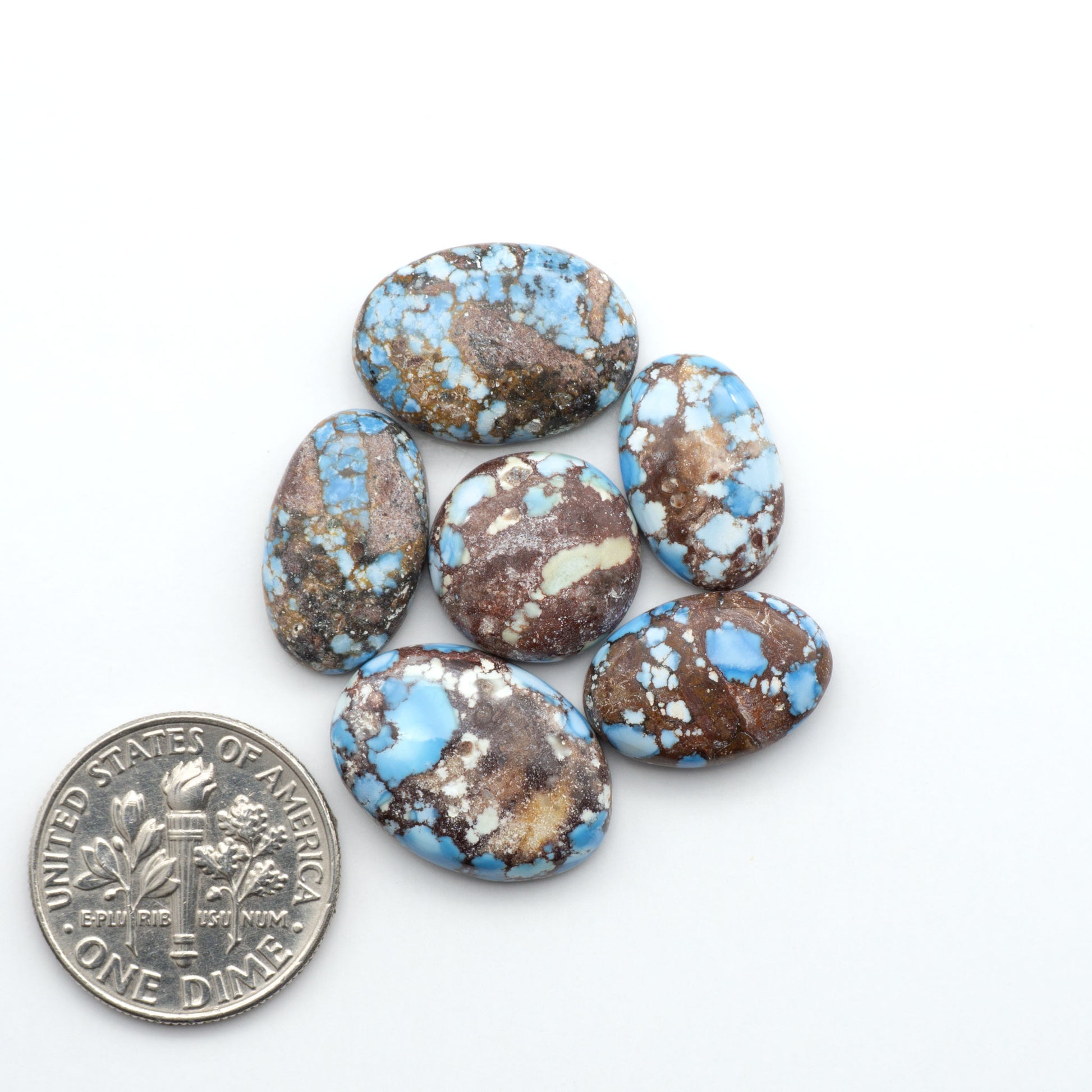 Golden Hills Turquoise cabochons, icy blue to lavender tones with chocolate matrix, polished stones on a white background with a US dime for scale