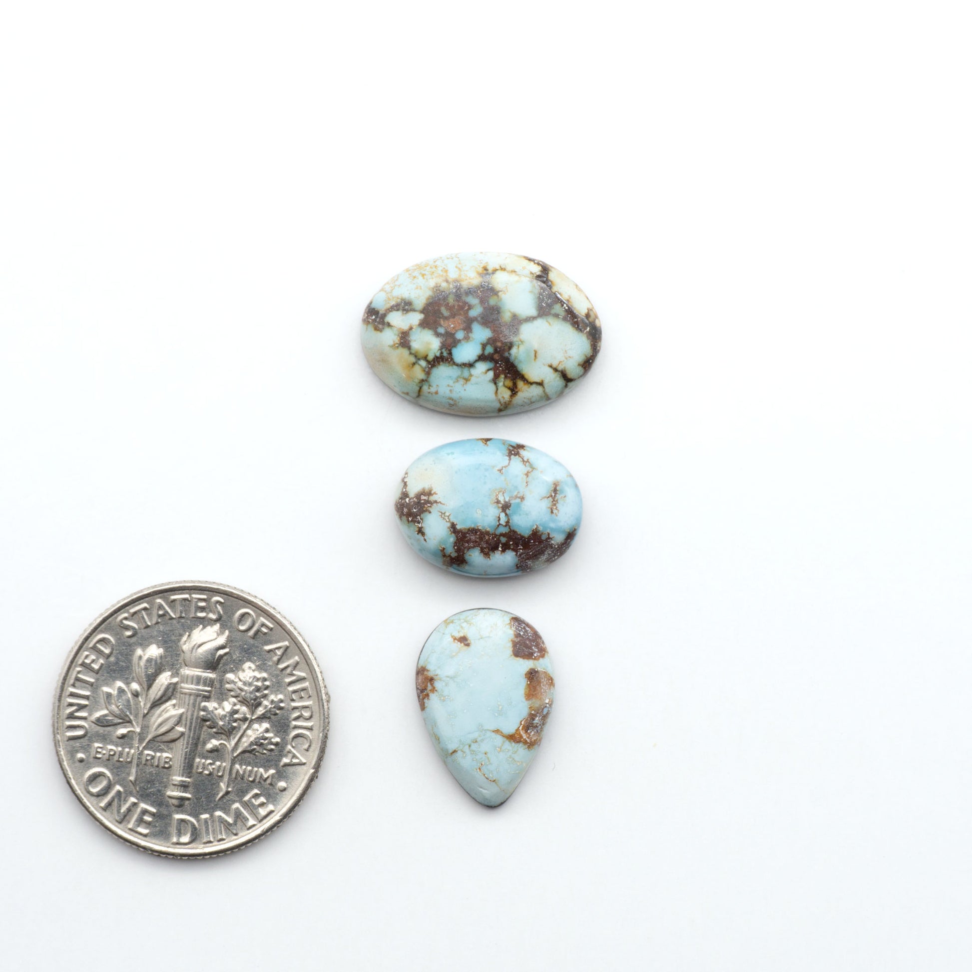 Golden Hills Turquoise cabochons, icy blue to lavender tones with chocolate matrix, polished stones on a white background with a US dime for scale