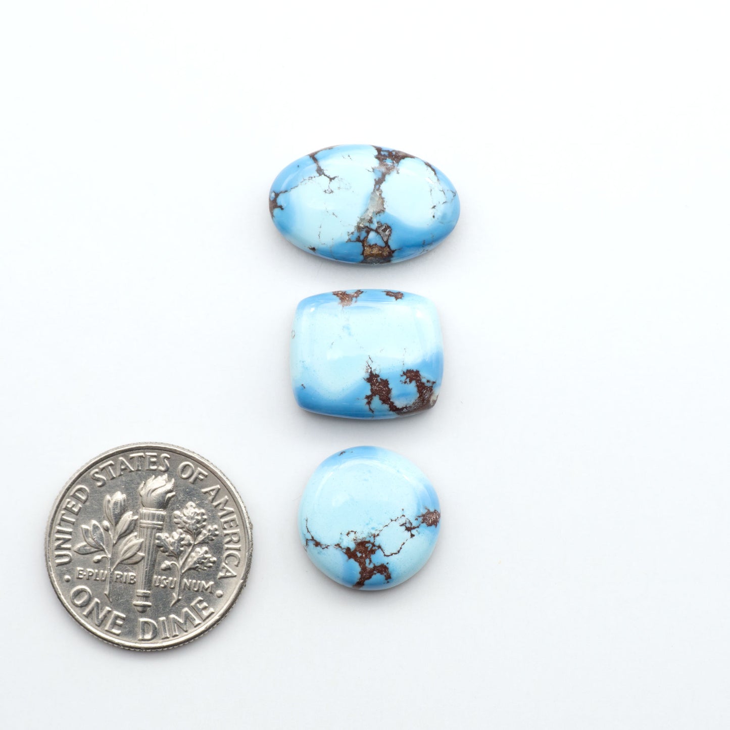 Golden Hills Turquoise cabochons, icy blue to lavender tones with chocolate matrix, polished stones on a white background with a US dime for scale
