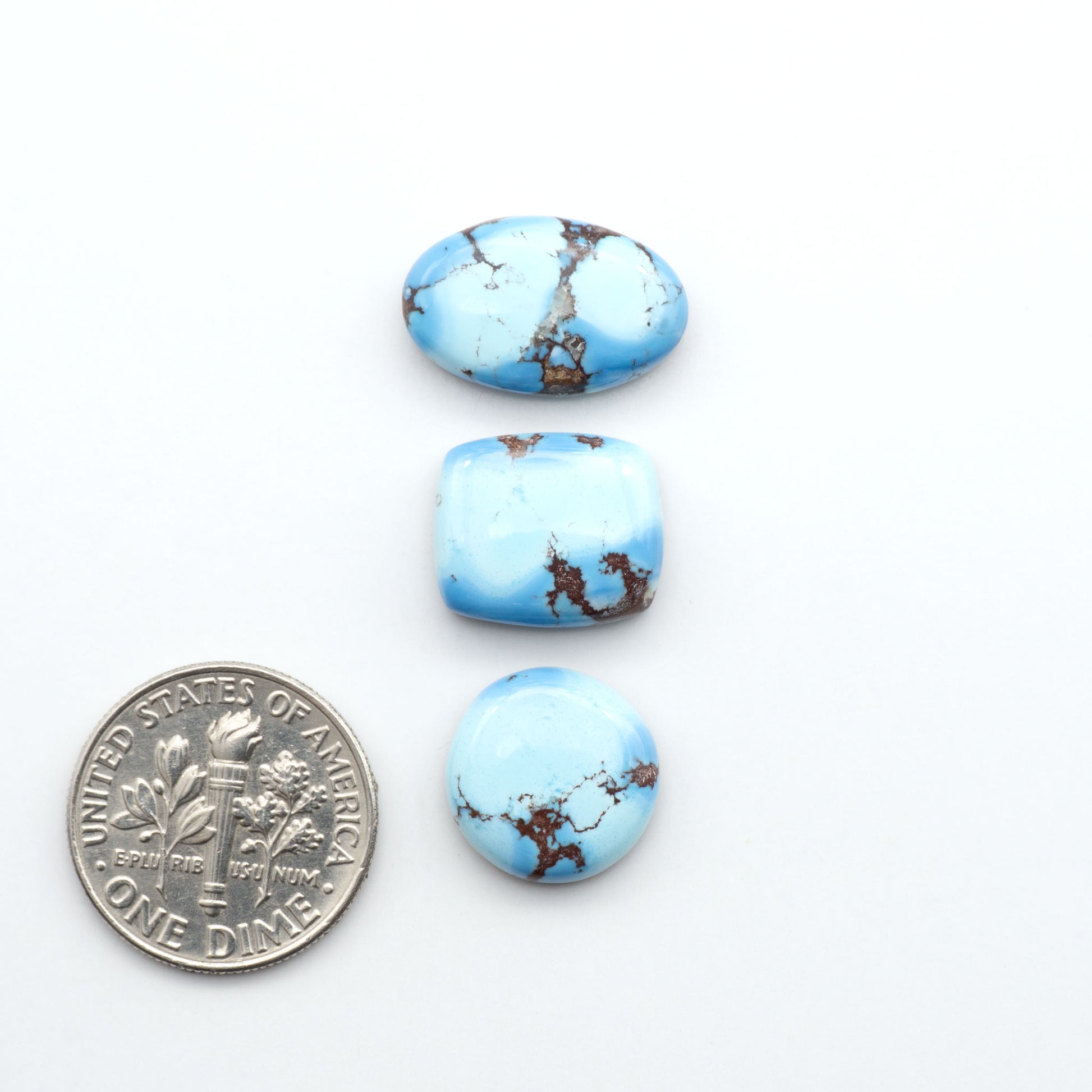 Golden Hills Turquoise cabochons, icy blue to lavender tones with chocolate matrix, polished stones on a white background with a US dime for scale
