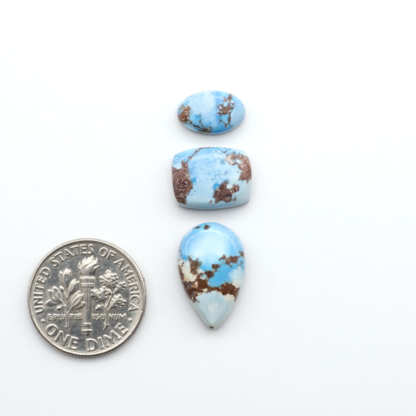 Golden Hills Turquoise cabochons, icy blue to lavender tones with chocolate matrix, polished stones on a white background with a US dime for scale