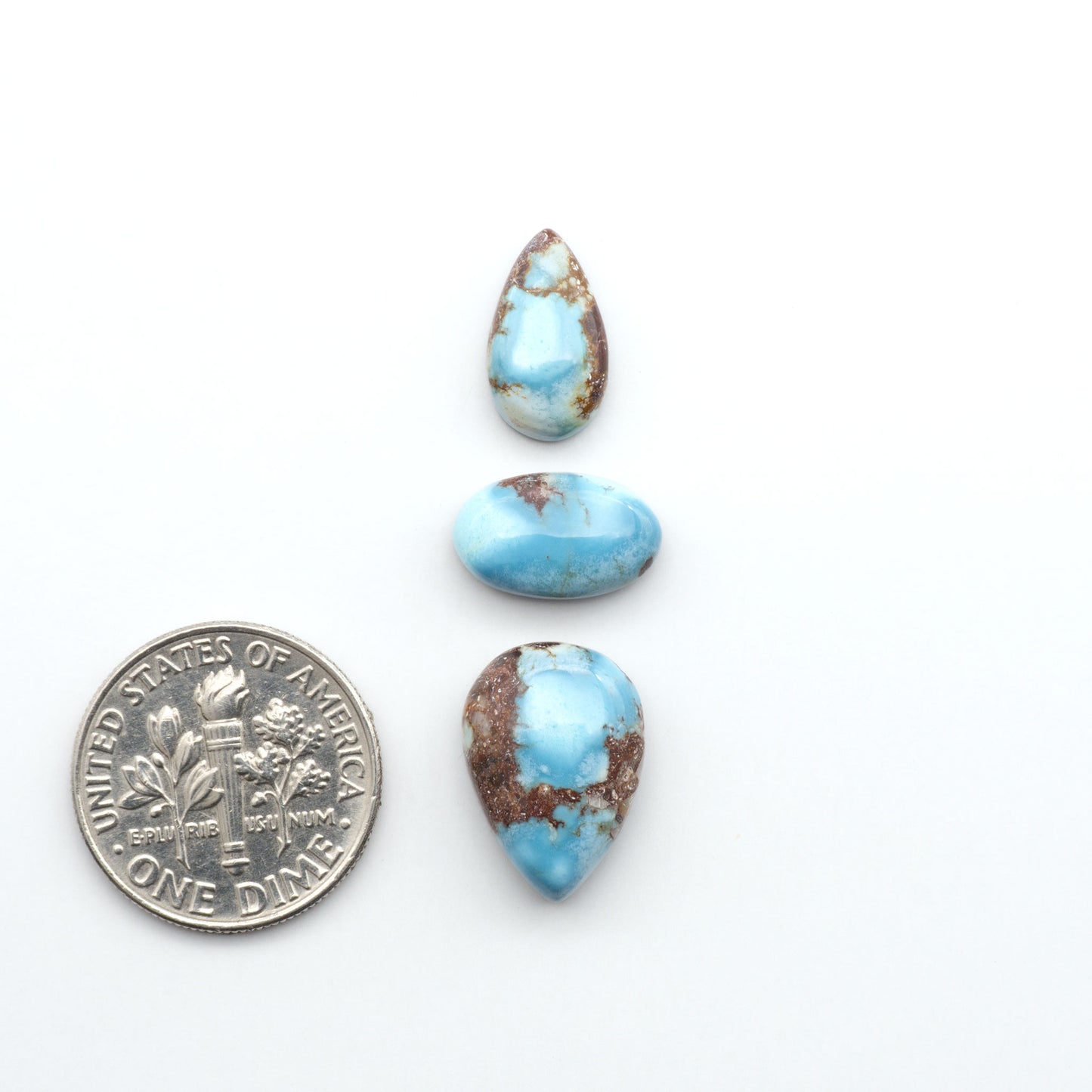 Golden Hills Turquoise cabochons, icy blue to lavender tones with chocolate matrix, polished stones on a white background with a US dime for scale