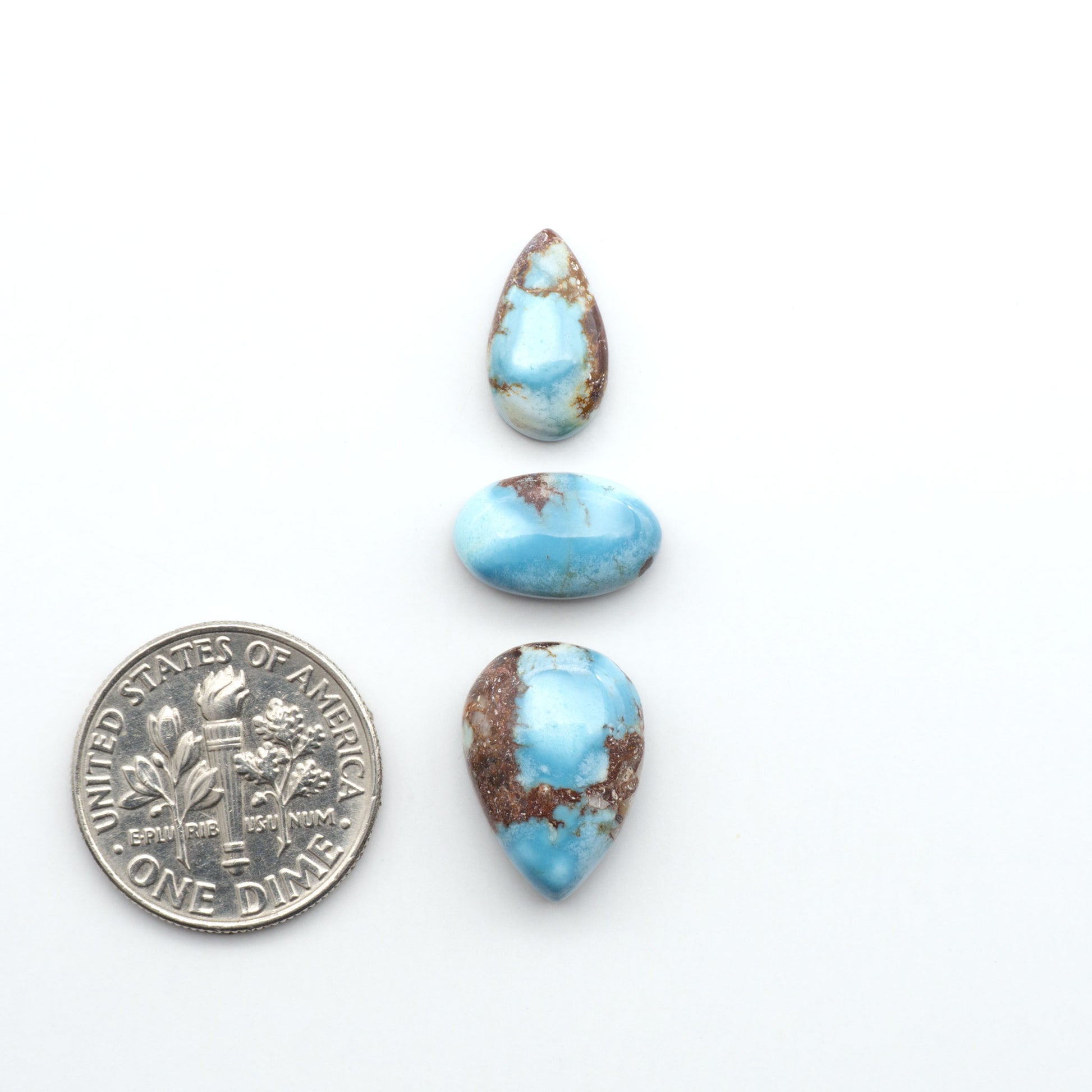 Golden Hills Turquoise cabochons, icy blue to lavender tones with chocolate matrix, polished stones on a white background with a US dime for scale