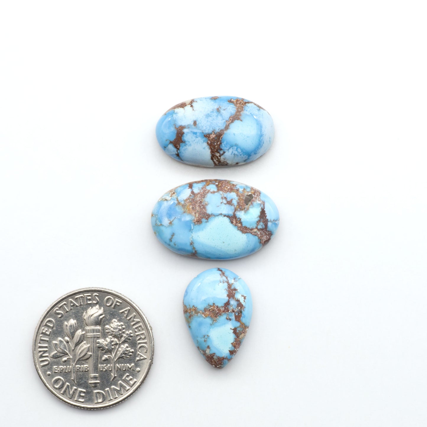 Golden Hills Turquoise cabochons, icy blue to lavender tones with chocolate matrix, polished stones on a white background with a US dime for scale
