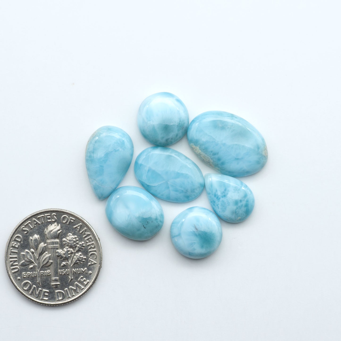 Larimar stone cabochons, cut and polished, blue and white gemstones on a white background, with a US dime for scale
